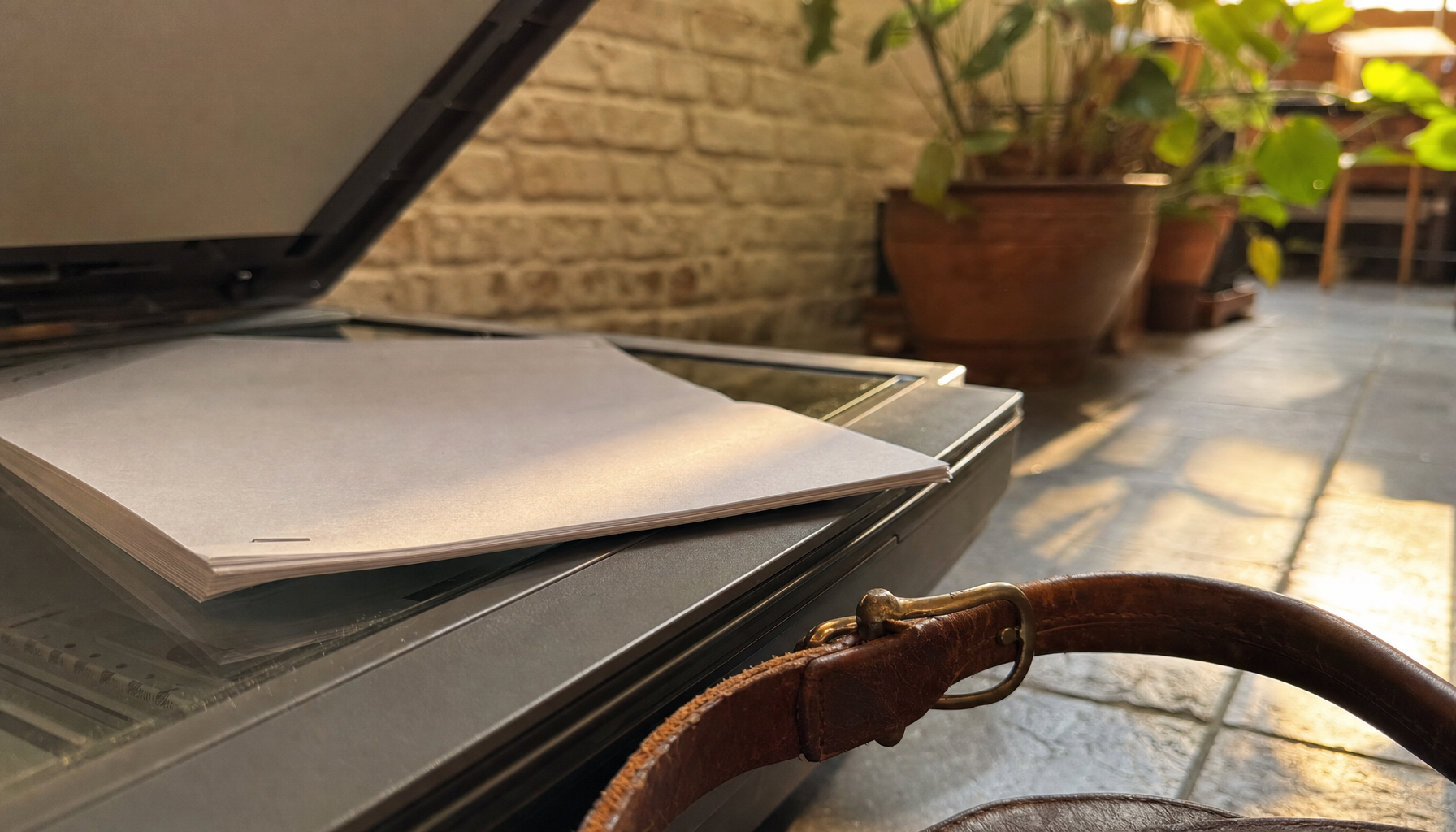Gros plan sur la vitre d'un scanner à plat ouvert où repose une liasse de pages agrafées posée face contre verre, lumière dorée de fin d'après-midi
